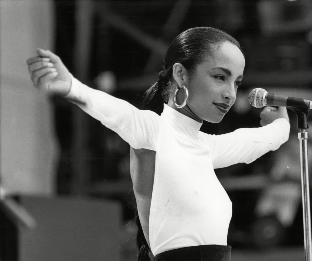 Čiernobiela momentka z koncertu Sade Adu v bielom roláku s výstrihom na chrbte.