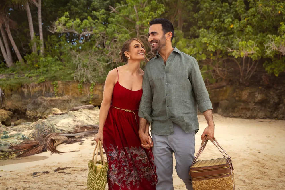 Jennifer Lopez v červených šatách a Brett Goldstein sa držia za ruky počas prechádzky na pláži vo filme Office Romance (Pracovní romance).
