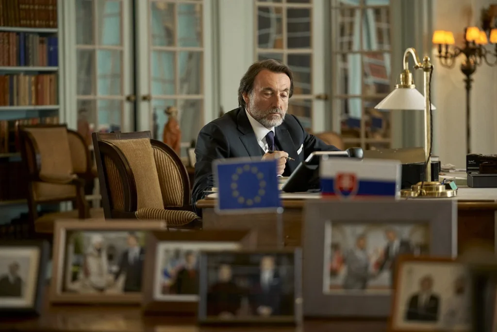 Expremiér Viktor Hudák v seriáli Víťaz pracuje za stolom s vlajkami Slovenska a Európskej únie.