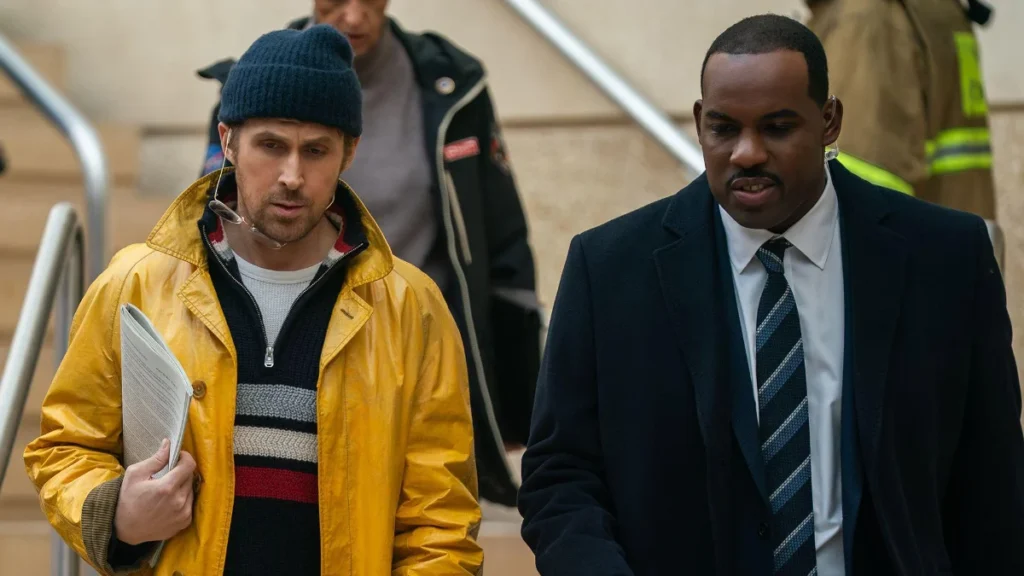 Herec Ryan Gosling v žltom kabáte a Lionel Boyce ako bezpečnostný dôstojník Carl vo filme Posledná šanca.